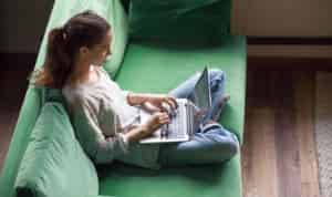 Woman sitting on couch, browsing through a catalog of blogging courses on her laptop
