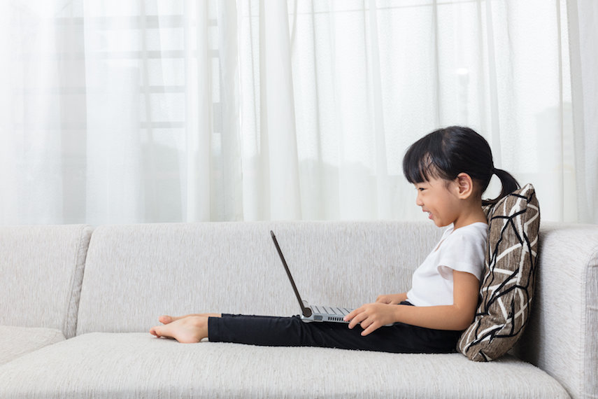 happy little Asian girl lying on sofa with laptop