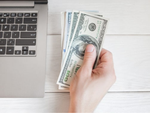 person holding cash next to laptop