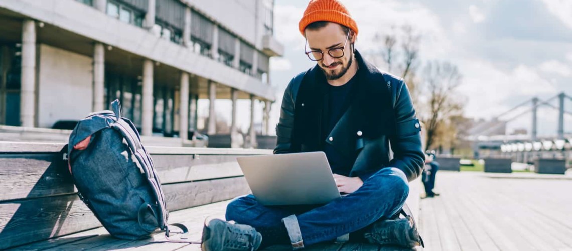 young man sitting on ground with backpack and laptop