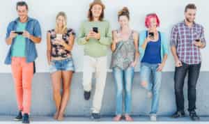 young people standing against a wall and looking at their phones