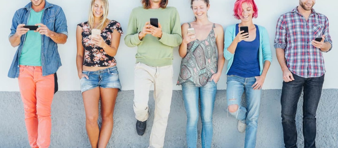 young people standing against a wall and looking at their phones