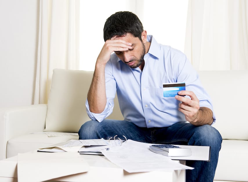 young latin american man sitting on sofa with credit card bills looking worried and stressed