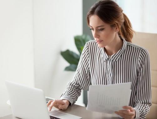 woman sorting through finances on paper and laptop