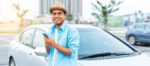 man standing by car holding smartphone