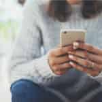 women in gray sweater using smartphone to make passive income
