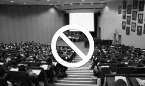 Black and white photo of a college classroom with caution symbol overlayed