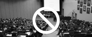 Black and white photo of a college classroom with caution symbol overlayed