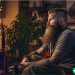 A bearded man in his 30s that is sitting on his couch playing video games.