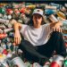 A teenager sitting in a huge pile of aluminum cans, almost as if he is showing off.