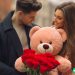 A boyfriend handing his girlfriend a stuffed bear and roses for Valentines day.