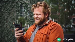 A large man looking down at a cell phone in his hand with a smile on his face. Greenery in the background.