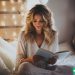 A woman sitting on her bed, reading a book.