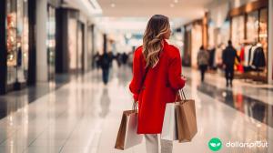 A woman in a red coat walking away from the camera in a shopping mall, holding several bags of merchandise.