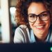 A close up shot of a woman wearing glasses in front of a laptop. She is working testing a new website.