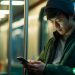 An Asian man on the subway watching videos on his phone.