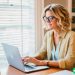 A blonde woman in her early forties who is writing an article on her laptop.