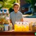 A 7 year old boy standing at his own lemonade stand on his neighborhood street.