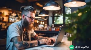 A hipster-looking guy making money from his laptop at a coffee shop.