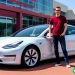 A man in his late twenties standing next to his white Tesla.