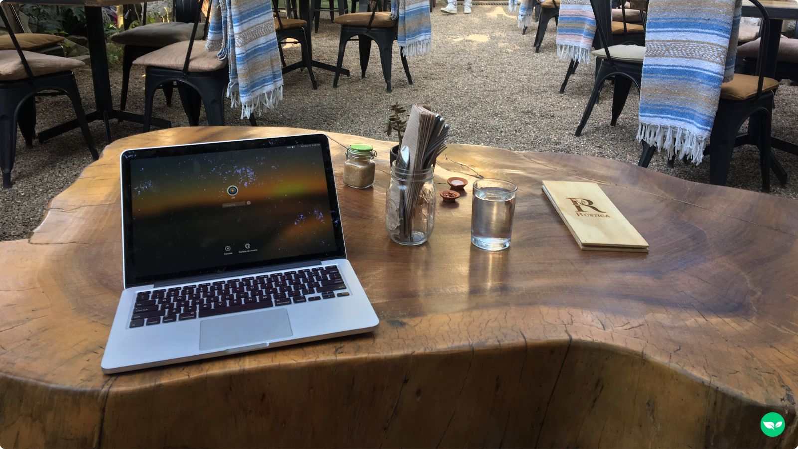 A laptop sitting on a natural wood table outside at a cafe.