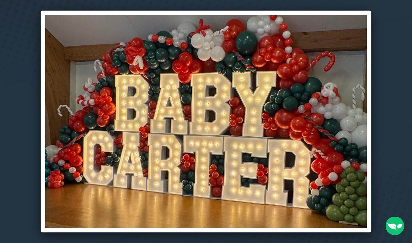 A vibrant balloon display with illuminated marquee letters spelling "Baby Carter," featuring red, green, and white holiday-themed décor.