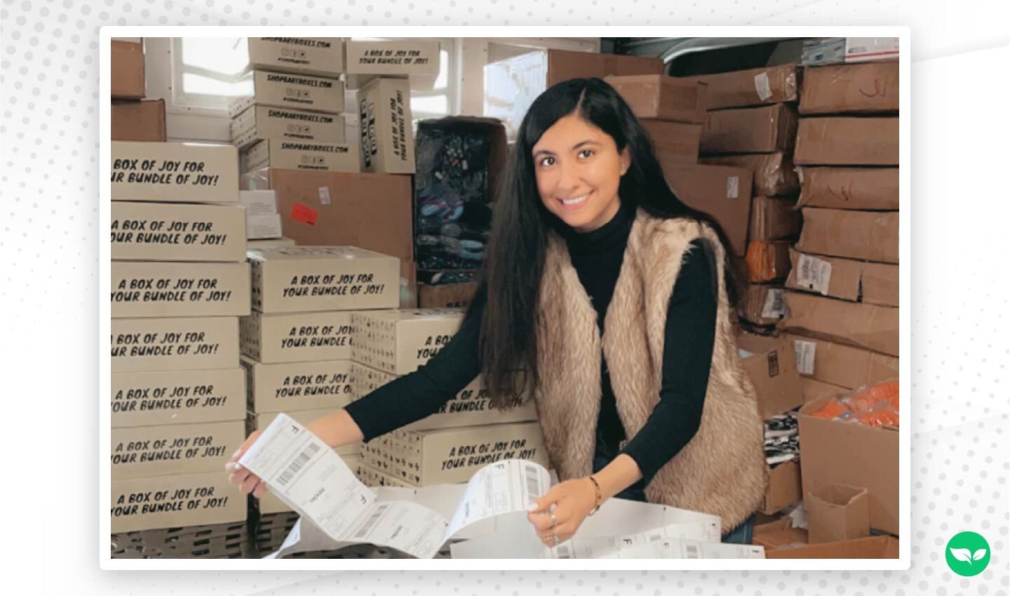 Zarina Bahadur smiling while preparing shipping labels in a warehouse filled with stacked 123 Baby Box packages.