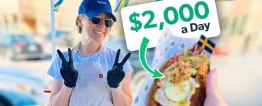 Amelia Eudailey, founder of Chef Hej Hej, smiling and flashing peace signs at her Swedish hot dog pop-up stand, with a fully loaded hot dog in the foreground.