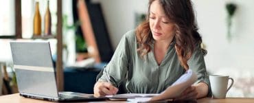 Woman working at a laptop with paperwork and coffee, representing the middle-class creator economy.