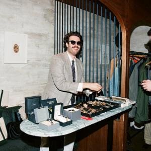 Aaron selling vintage watches from a pop-up setup, arranging timepieces and watch boxes while talking with a customer.