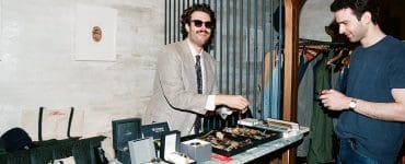 Aaron selling vintage watches from a pop-up setup, arranging timepieces and watch boxes while talking with a customer.